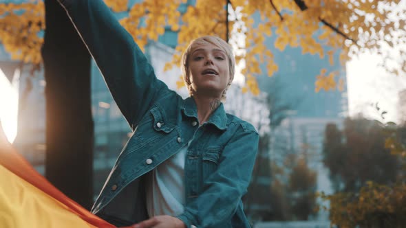 Beutiful Young Woman with Short Blond Hair Spinning the Rainbow Flag Around Herself in the Park in