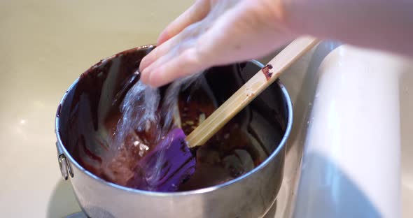 A chef cleaning up in the sink washing a mixing bowl and spatula that are covered in chocolate cake