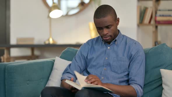 Young African Man Reading Book on Sofa
