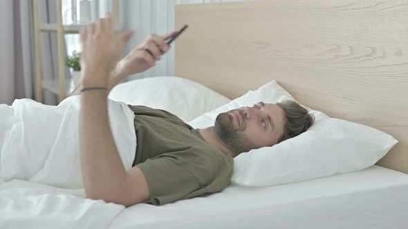 Young Man Talking on His Cellphone in Bed
