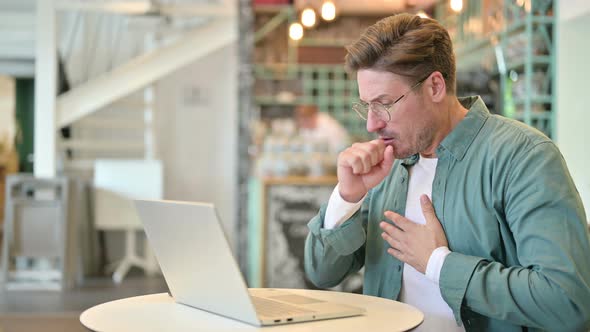 Sick Middle Aged Man with Laptop Coughing in Cafe 