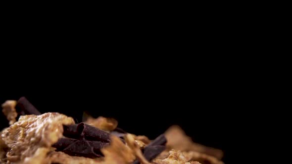 Chocolate chips with dry wheat flakes falling in slow motion on a black background. Macro