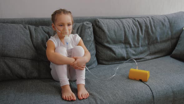 Little Girl Makes Inhalation with Medical Nebulizer While Sitting on Bed