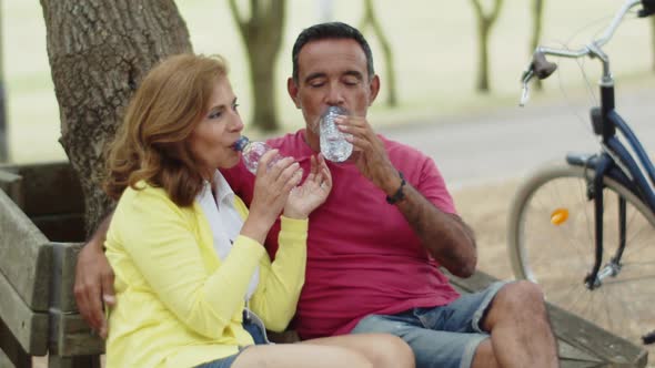 Senior Couple Drinking Water in Park After Cycling