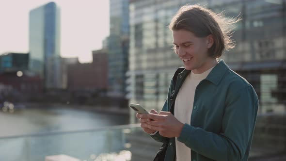 Happy Young Guy Walking on Street and Texting on Smartphone