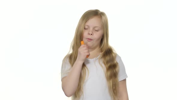 Little Girl Eats a Carrot and Shows a Thumbs Up. White Background