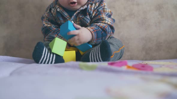 Cute Boy Plays with Bright Cubes Sitting on Large Soft Bed