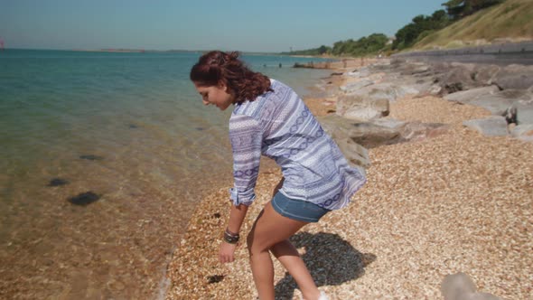 Close Up Shot Of Young Woman Reaching Down To Pick Up Plastic Bottle On Beach In Slowmotion