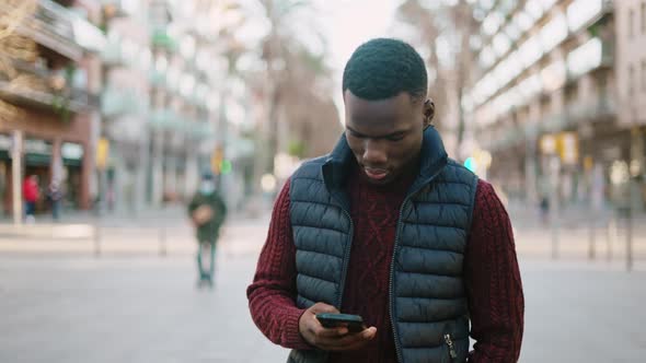 Black Man Browsing Smartphone and Walking in City