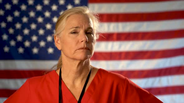 Medium tight portrait of nurse looking extremely worried and sad with American flag behind her.