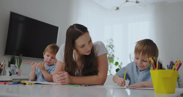 A Young Mother with Two Children Sitting at a White Table Draws Colored Pencils on Paper