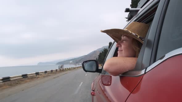  woman looking at sea from car window while driving on road.