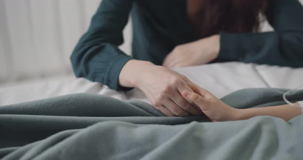 Close Up of Mother Holding Hand of Sick Child Having Dropper and Lying in Bed at Hospital