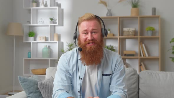 Young Redhead Man in Headphones Looks at Camera Makes Speech Negotiate Use Video Conference App and