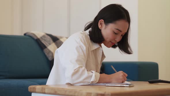 Smiling Asian woman writing something and looking to the side