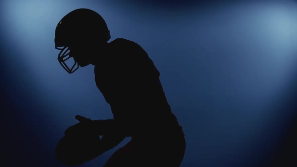 Silhouette of Professional Male American Football Player in Helmet Holding a Ball Walking Against
