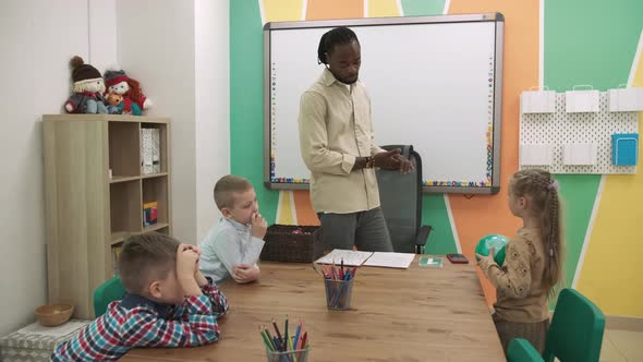 An African American Teacher Teaches a Group of Children in the Classroom in a Playful Way