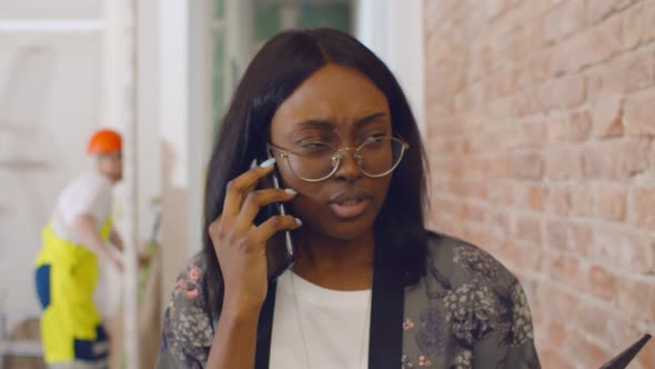 Young African Woman Designer Talking on Phone with Client Standing in Apartment Being Renovated