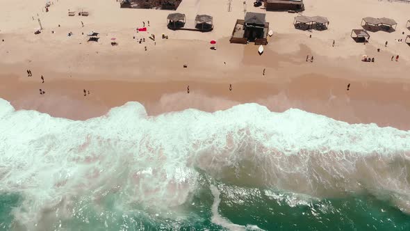 Static aerial drone showing endless wild sea waves breaking on the sandy coast line while people han