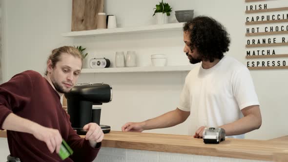 A young customer pays for a purchase with a credit card through a bank terminal in a modern cafe