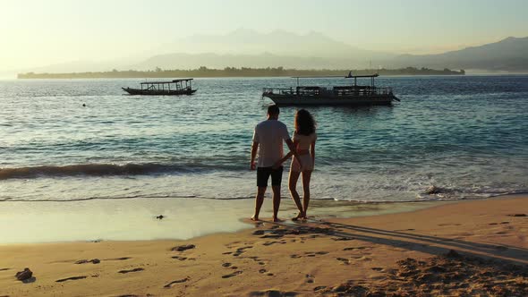 Young couple hugging, standing in front of twilight panorama with calm sea washing their feet under