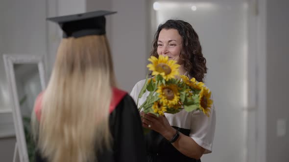 Smiling Happy Proud Mother Giving Bouquet of Yellow Sunflower to Graduate Daughter Talking