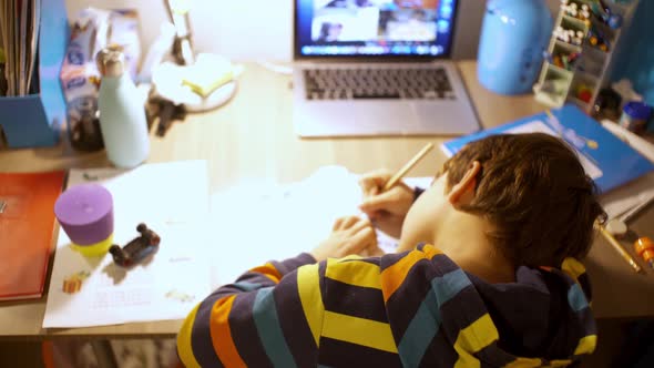 Back view of caucasian six year's old boy, studying at his desk with distance education system durin