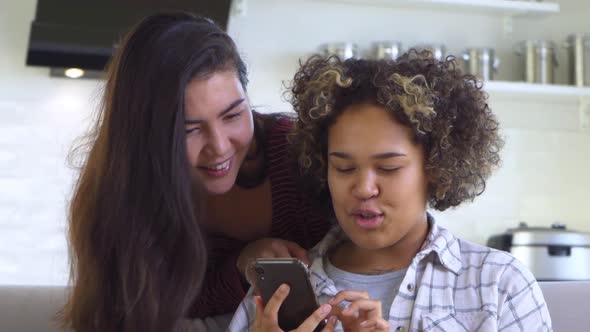 A Girl Hugs Her Friend From Behind Who is Holding a Smartphone