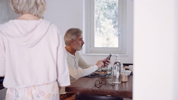 Mature couple during breakfast, man using smartphone