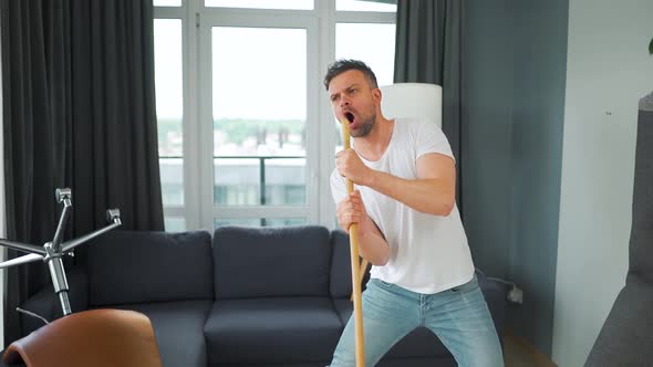 Man Cleaning the House and Having Fun Dancing and Singing with a Broom