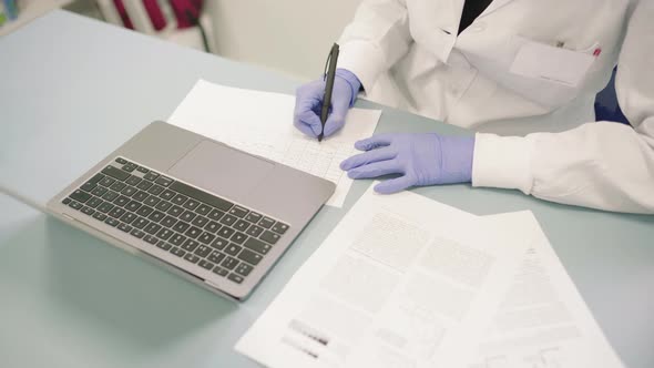 Woman Sitting On Table With Laptop And Papers Transcribing Analysis Results. - high angle