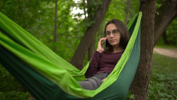 A Young Woman Swings in a Hammock and Talks on the Phone