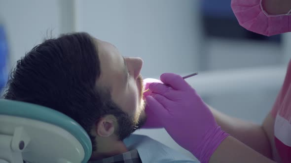 Dentist in Medical Mask and Gloves Checking the Tooth of the Patient Using Medical Tools