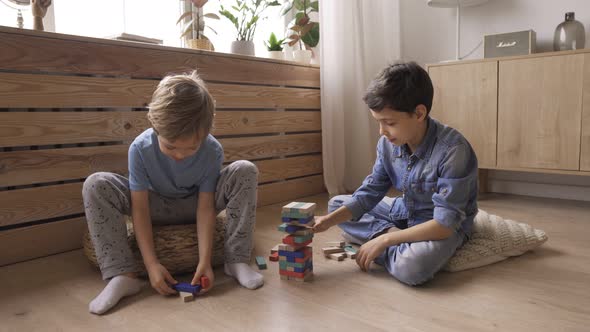 Two Boys Brothers Are Building a Tower From Wooden Blocks Sitting on the Floor