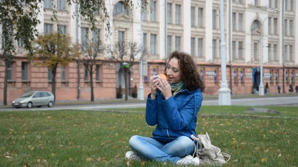 Beautiful Student Girl Eats a Hamburger or Cheeseburger on the Lawn