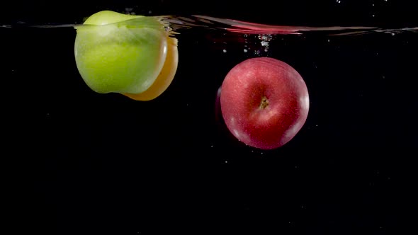 Beautiful yellow, green, and red apples floating in water in slow motion.