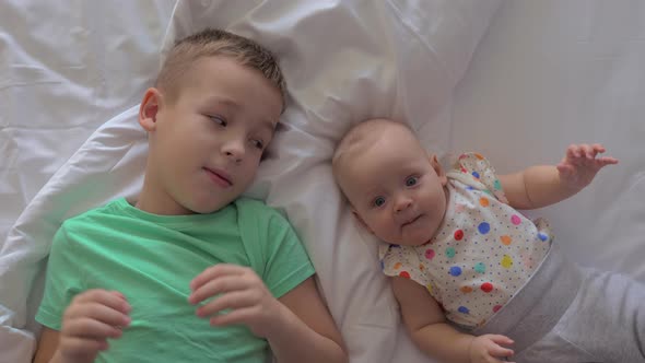 A Brother and a Baby Sister Lying on a Bed Close To Each Other