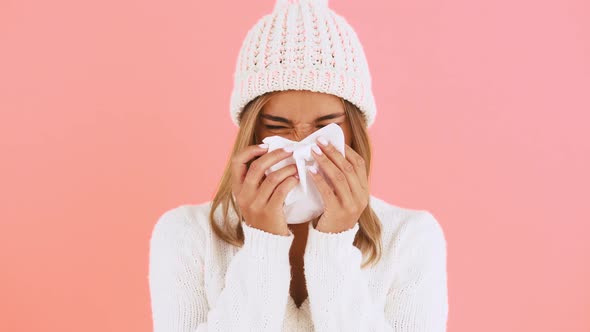 Young Female in Jumper and Hat is Wiping Her Runny Nose with a Tissue Smiling While Posing Against