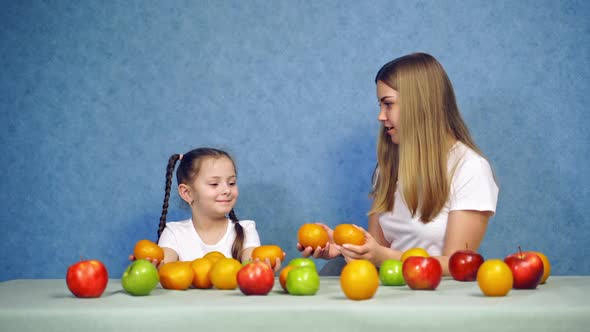 Woman and little girl playing with fresh fruits at home. 