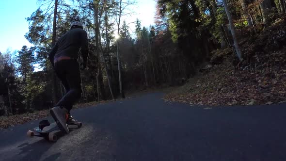 POV of young men longboard skateboarding downhill on a rural road