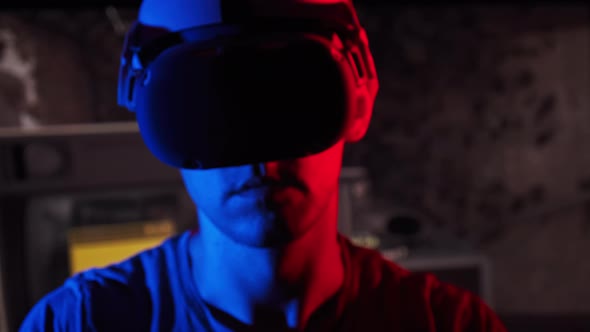 Man in a Virtual Reality Helmet Illuminated in Red and Blue Plays a Game