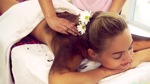 Relaxed Woman Lying on Spa Bed for Body Scrubbing Massage Using Traditional Herb