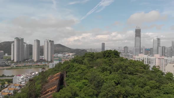 Slow pan reveal of Macau city skyline over the top of a mountain in Taipa