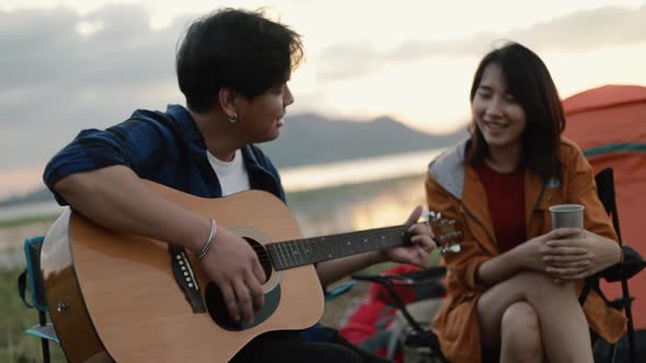 A happy young Asian couple backpacker playing the guitar and singing a song together.