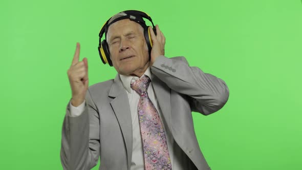 Funny elderly senior businessman in suit listens to music in headphones and dances. Chroma key