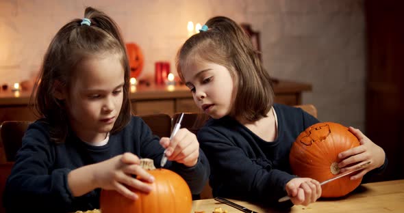 Two Cute Little Girls Are Cutting a Pumpkin on the Table for Halloween