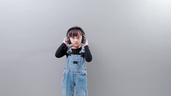 Cute Asian girl wearing headphones enjoy listening to music and dancing happily in studio.