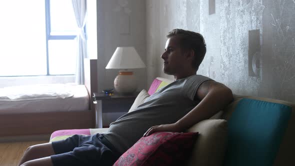 Handsome Young Man at Home Sitting on a Couch Watches TV