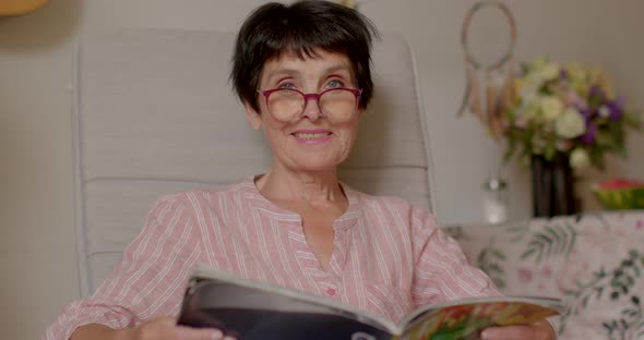 Woman of Retirement Age Reads a Magazine While Sitting in Cozy Armchair at Home