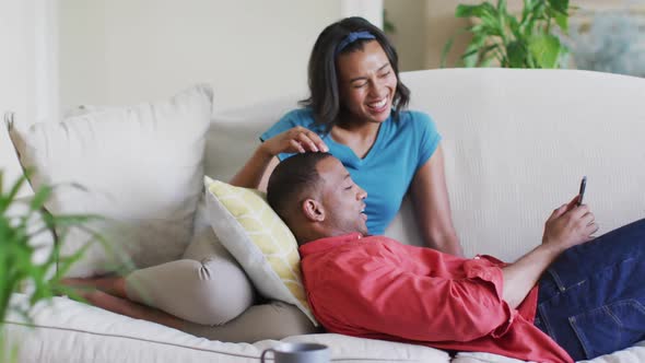 Happy biracial couple on sofa with smartphone and talking